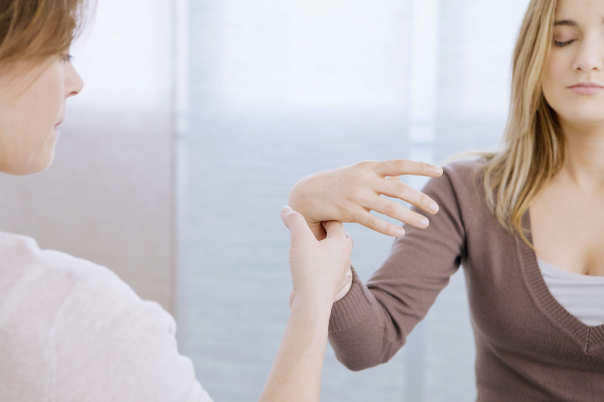A hypnotherapist guiding a client's raised arm as she rests in trance with her eyes closed